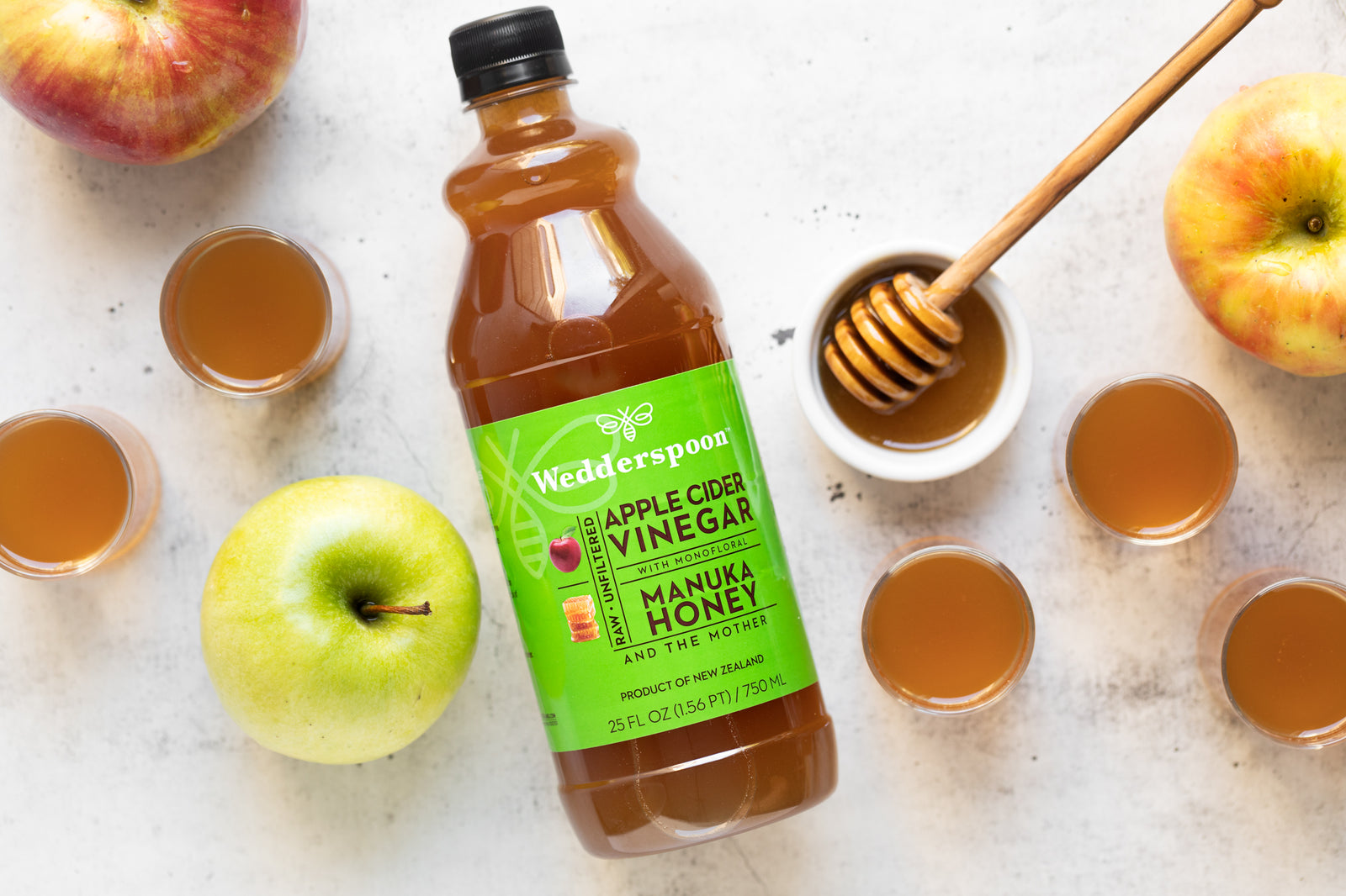Wedderspoon apple cider vinegar benefits shown with bottle, honey dipper, apples, and poured glasses on table