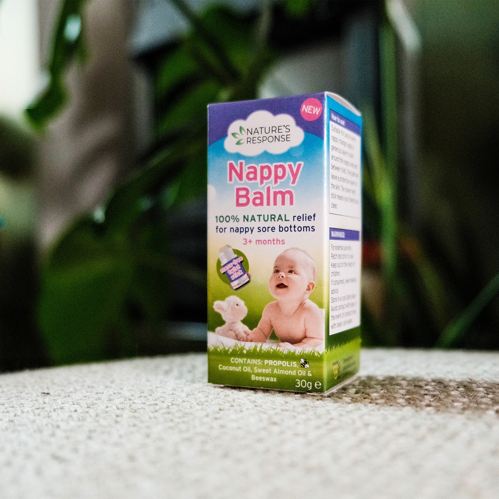 Box of Nappy Balm for babies on a textured surface with a blurred green background
