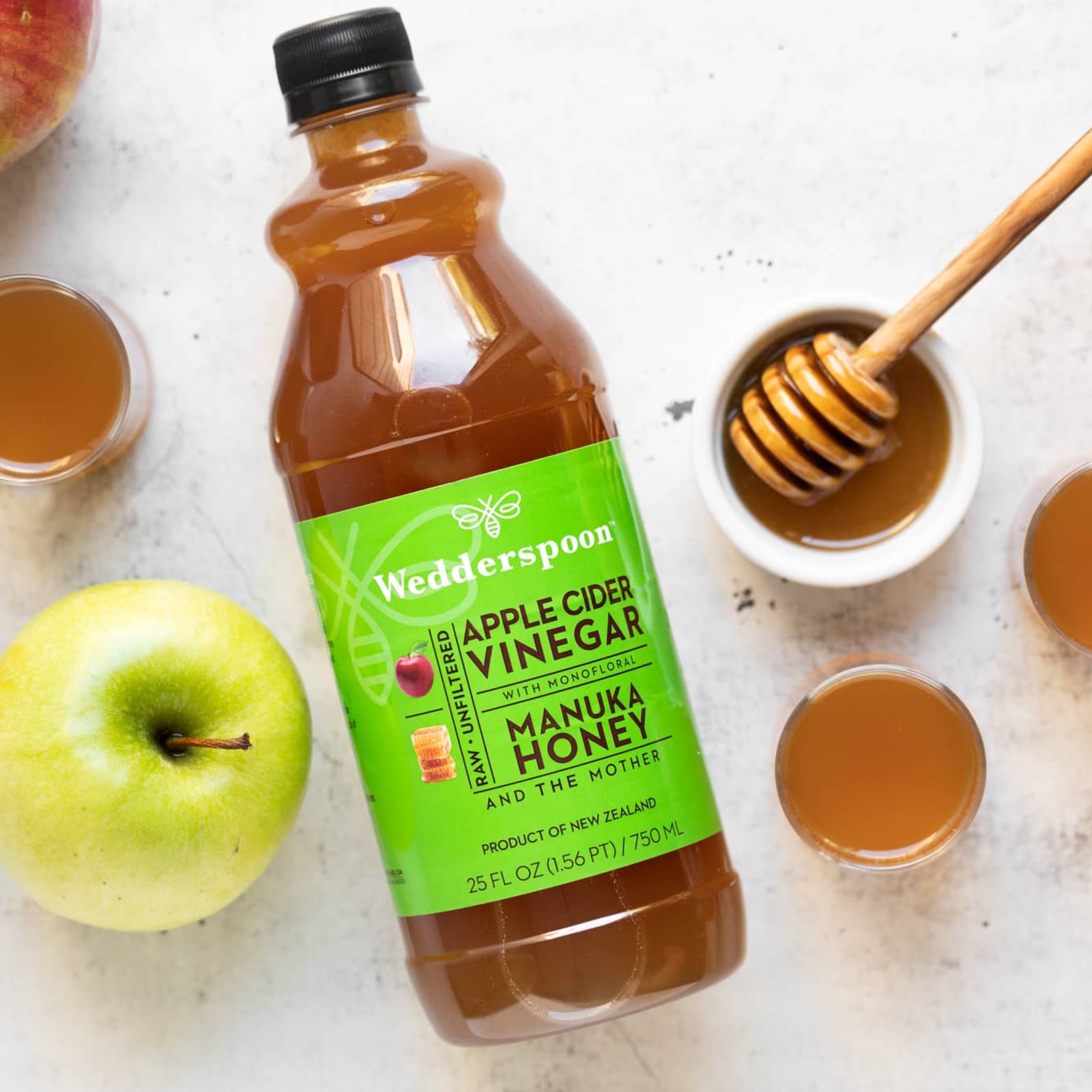 Wedderspoon Apple Cider Vinegar with Honey on a white surface with apples and honey.