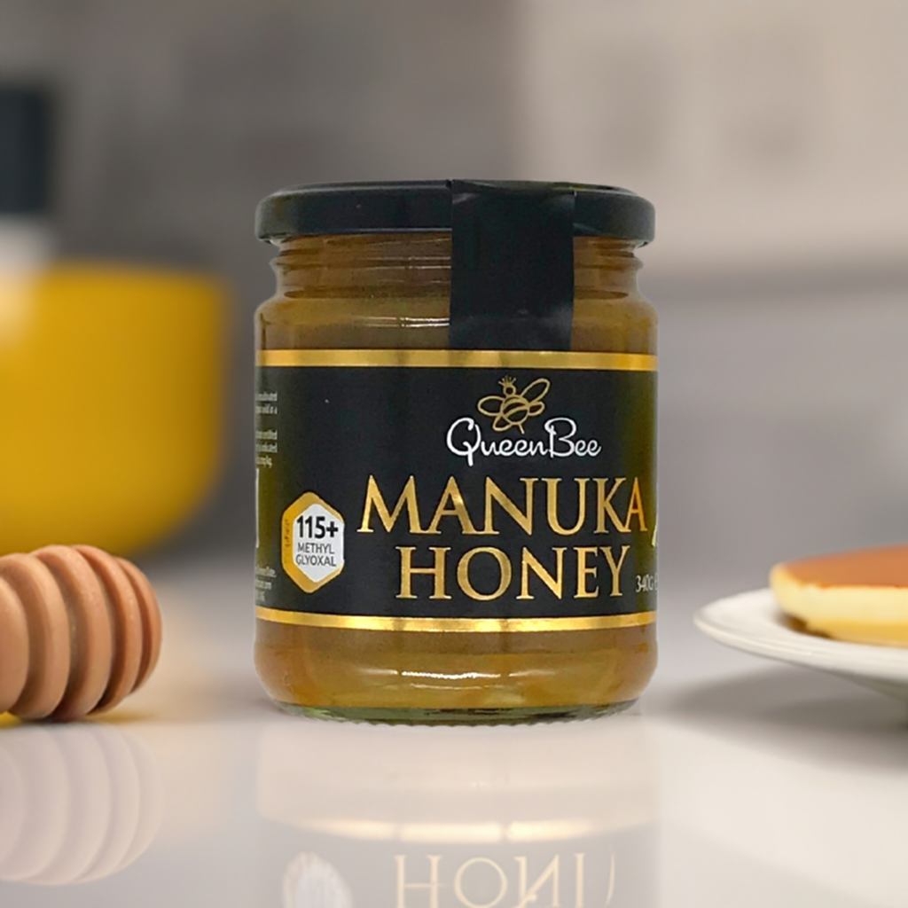 Jar of Queen Bee Manuka honey MG115 with 115 plus methylglyoxal on kitchen counter near honey dipper