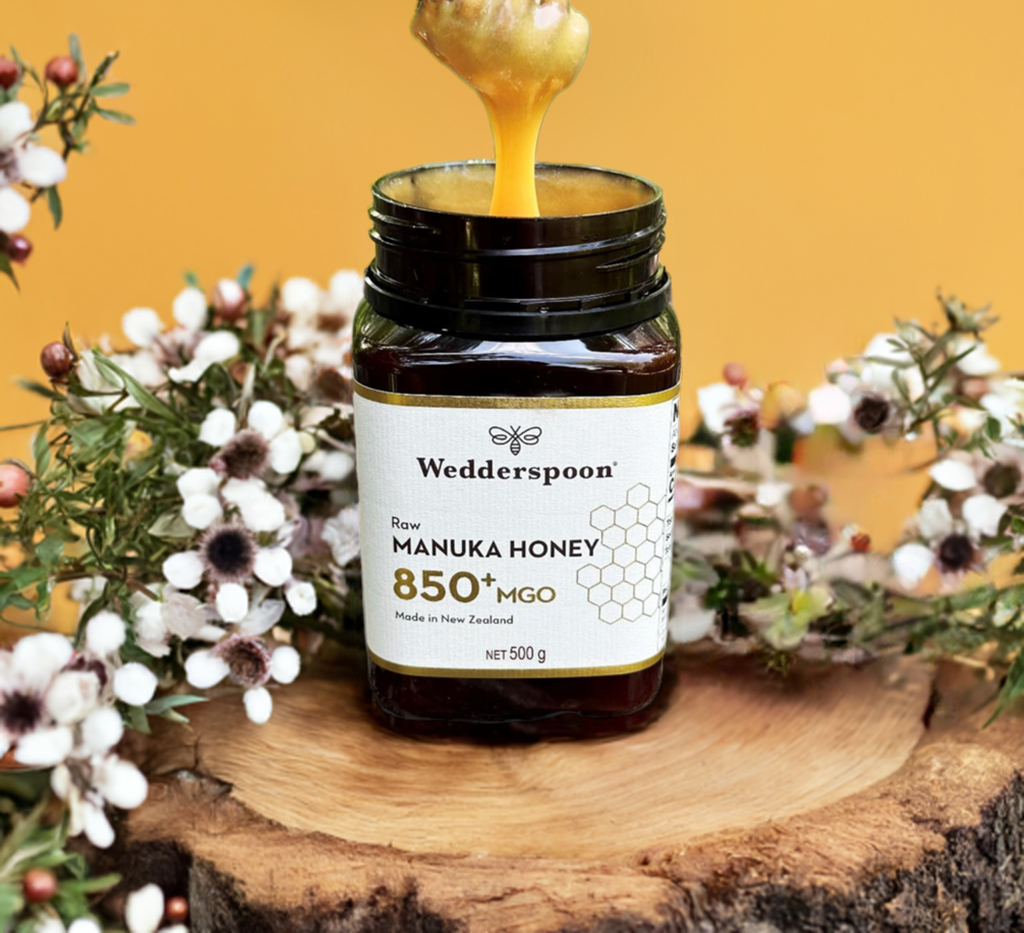 Wedderspoon raw manuka honey 850 mgo jar with honey dripping on wooden surface and flowers