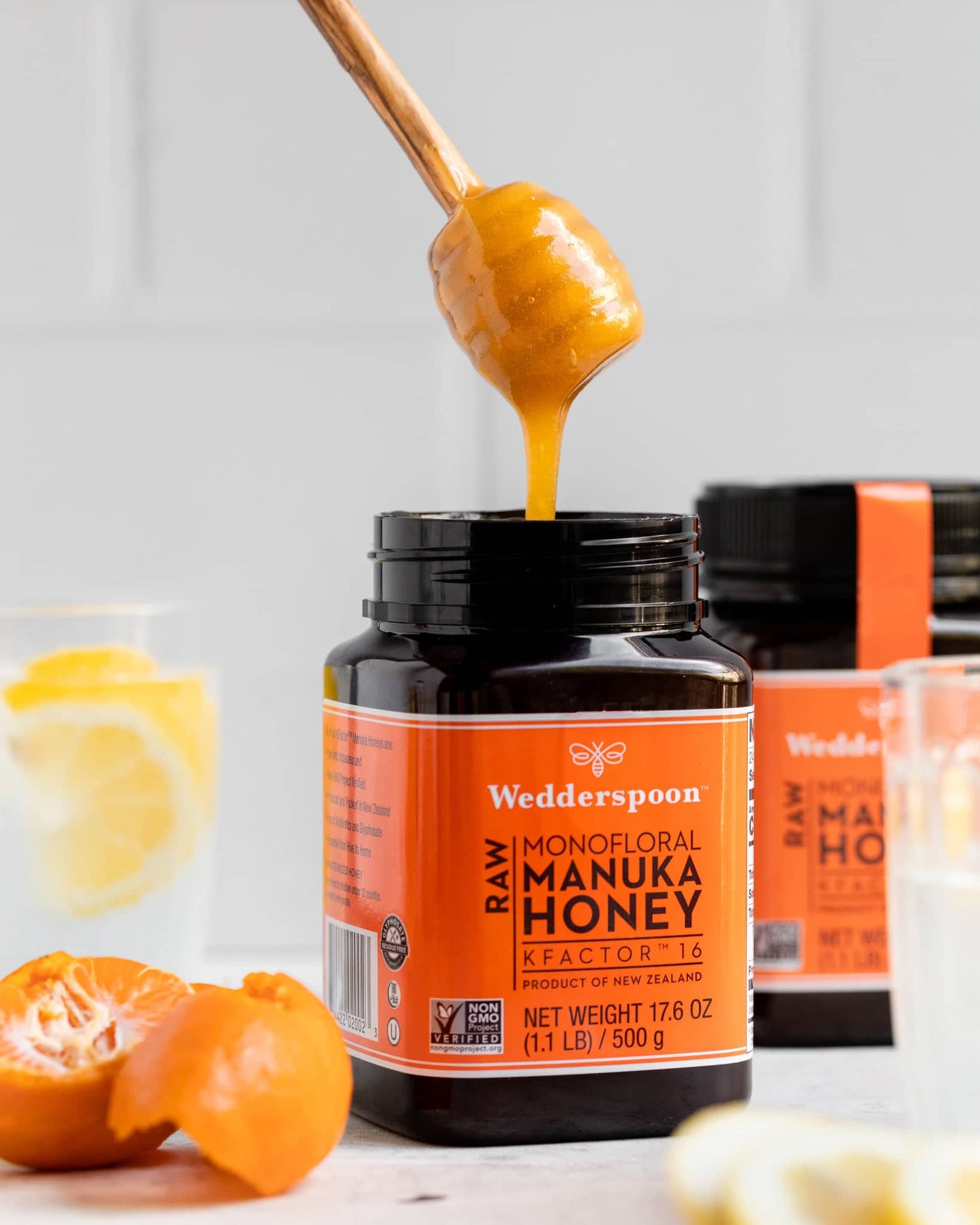 Jar of Wedderspoon raw Manuka honey KFactor 16 with a honey dipper and lemon slices