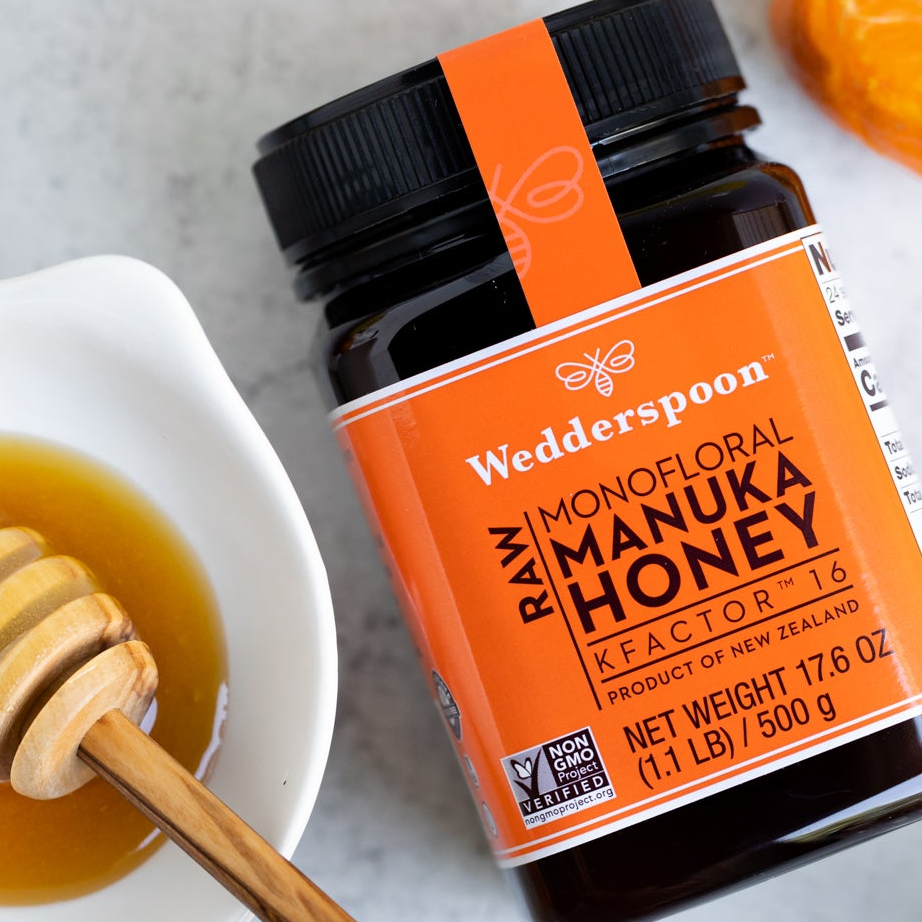 Wedderspoon raw Manuka honey KFactor 16 jar with honey dipper and bowl on a counter