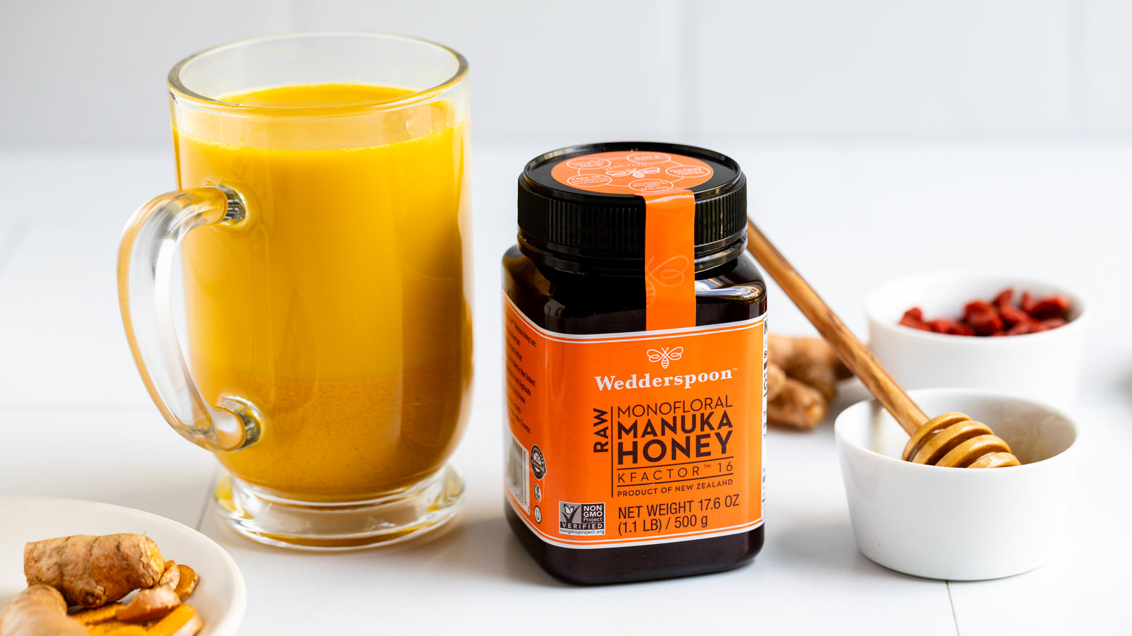 Wedderspoon raw Manuka honey KFactor 16 jar with turmeric tea and honey dipper on white background