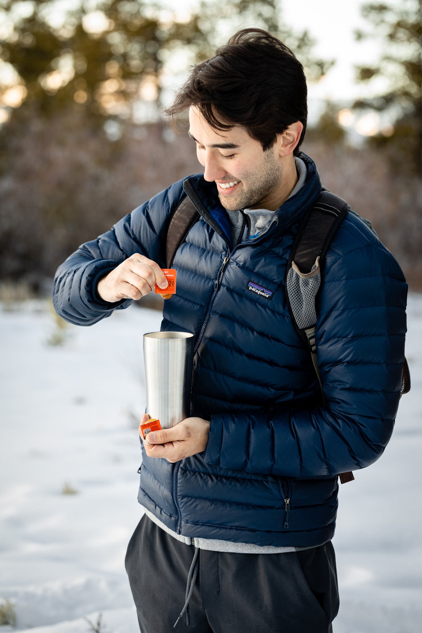 Man adding Wedderspoon raw Manuka honey travel sachets into a thermos outdoors in winter