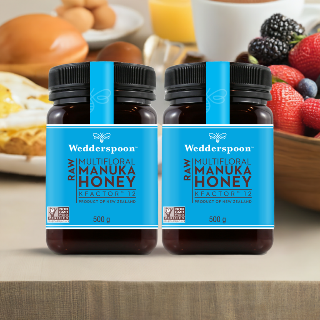 Two jars of Wedderspoon KFactor 12 honey raw multifloral Manuka honey 500g with breakfast in background