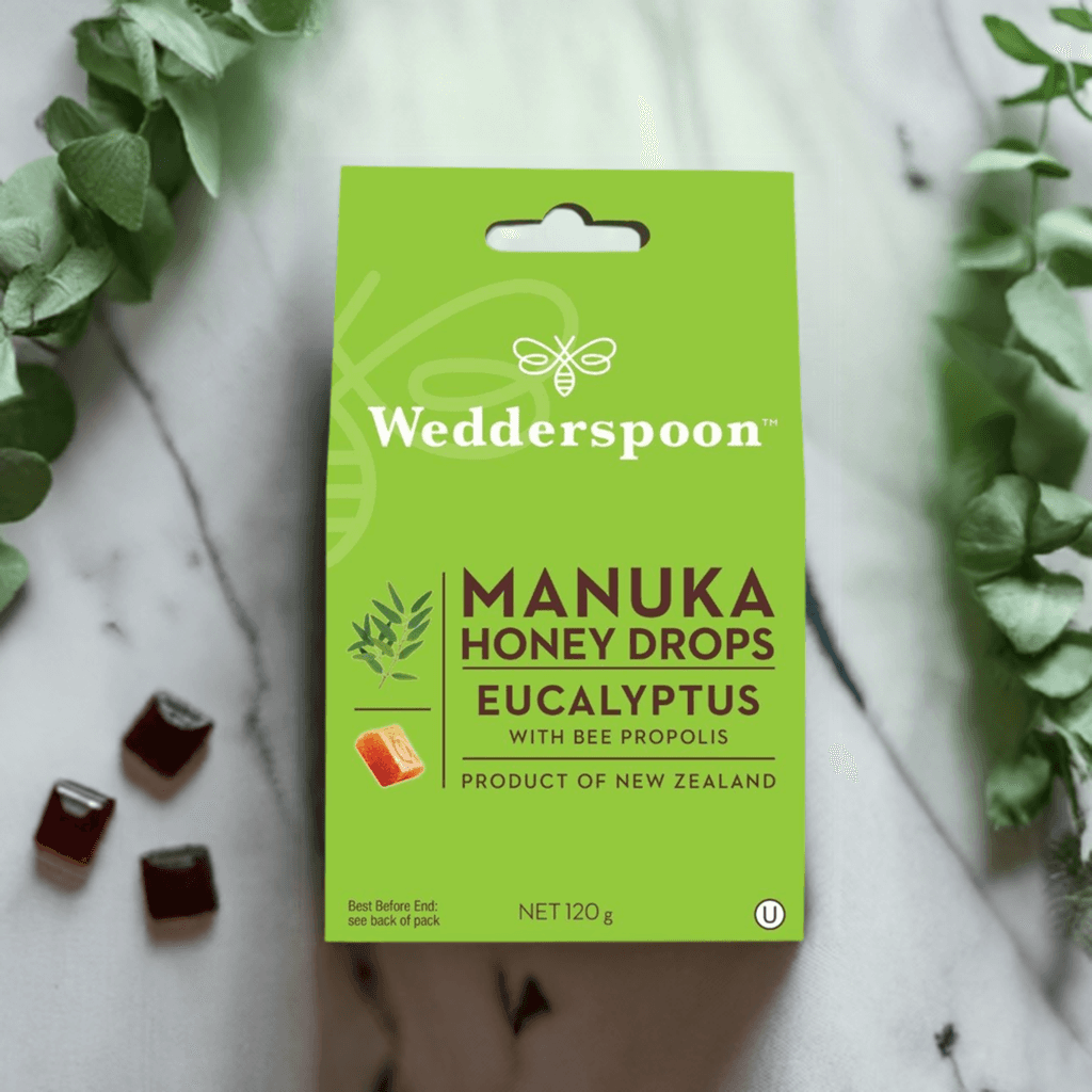 Wedderspoon Manuka honey drops eucalyptus throat lozenges in green box with eucalyptus sprigs and scattered lozenges