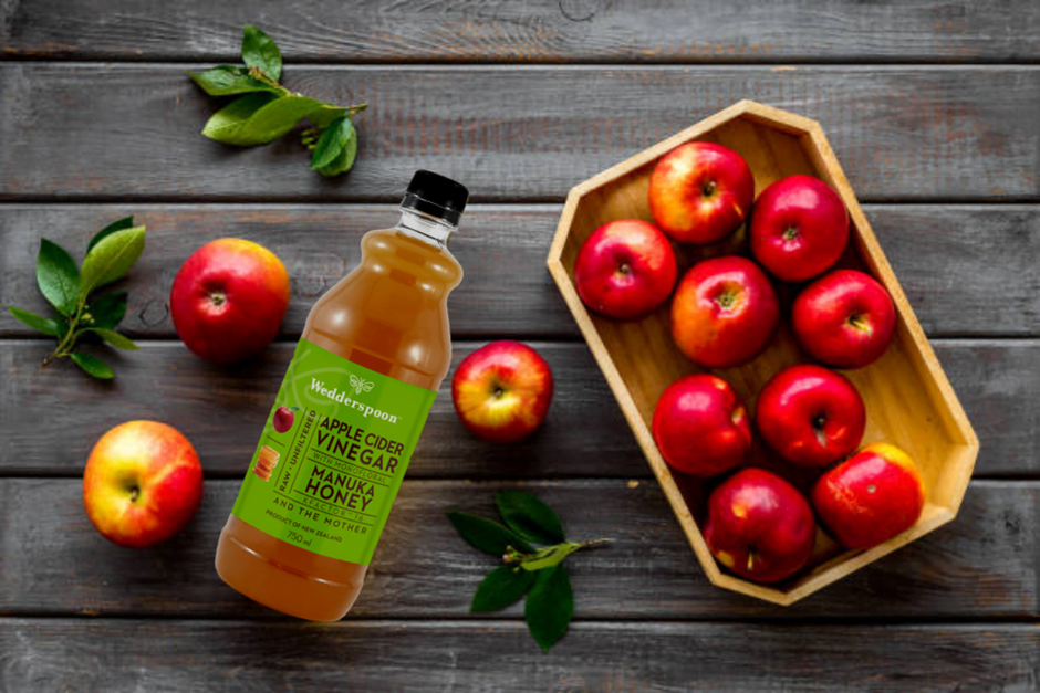 Bottle of apple cider vinegar for digestive health surrounded by fresh red apples on wooden surface