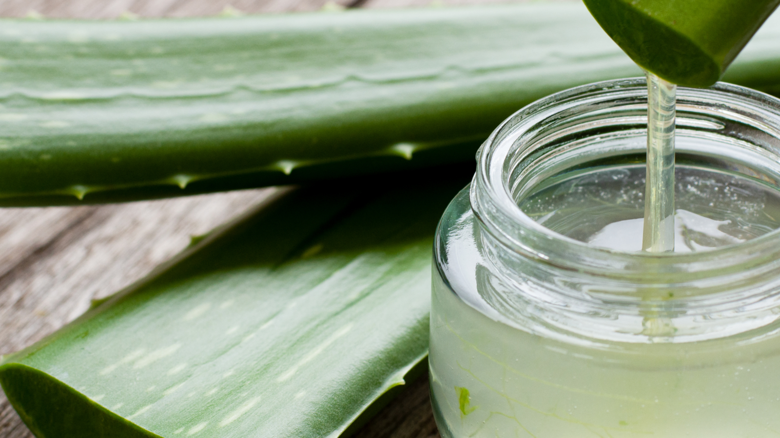 Jar of aloe vera gel with fresh aloe leaves on a wooden surface