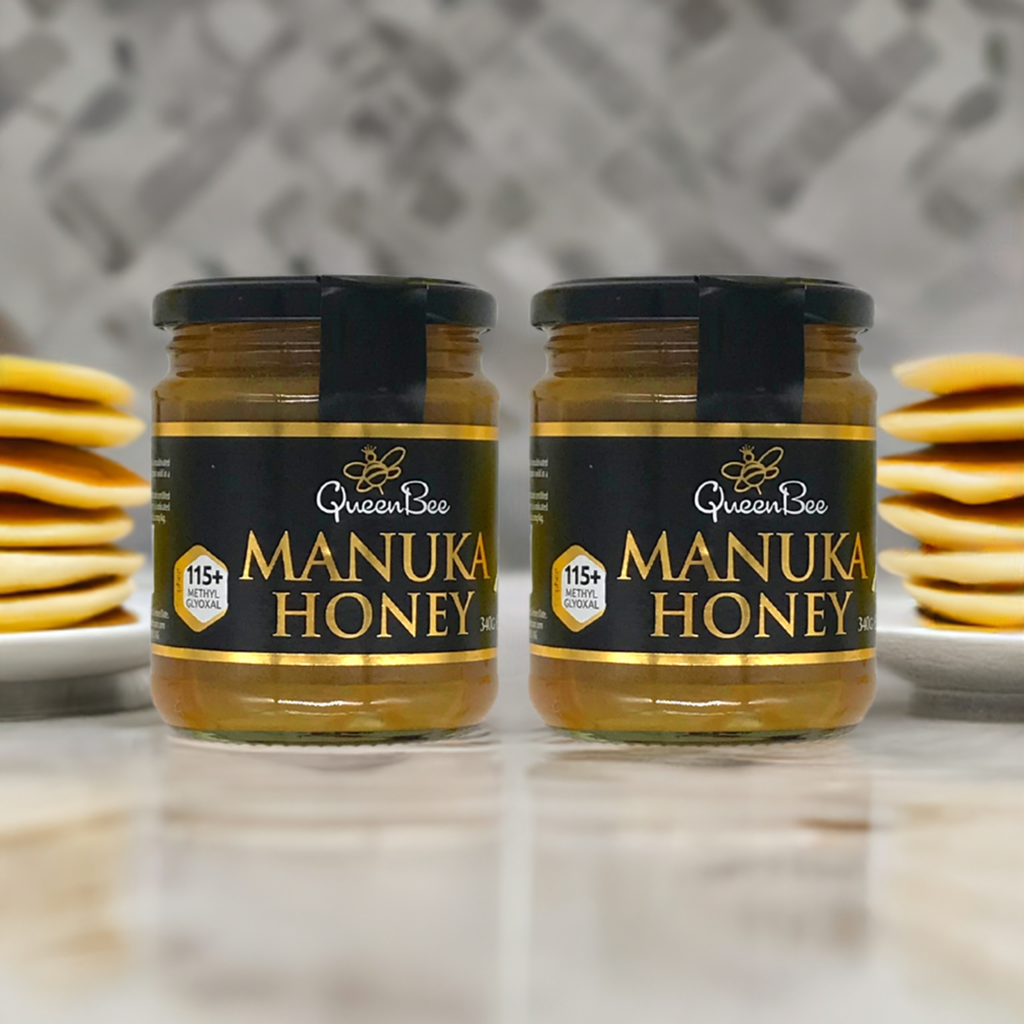 Queen Bee Manuka honey twin pack jars on marble surface with stacked pancakes in blurred background for breakfast