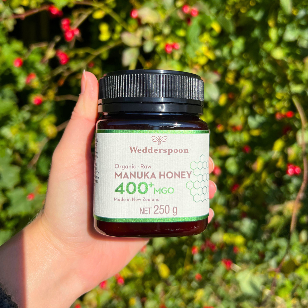 Wedderspoon high potency raw manuka honey 400 MGO jar 250g held in hand with garden background