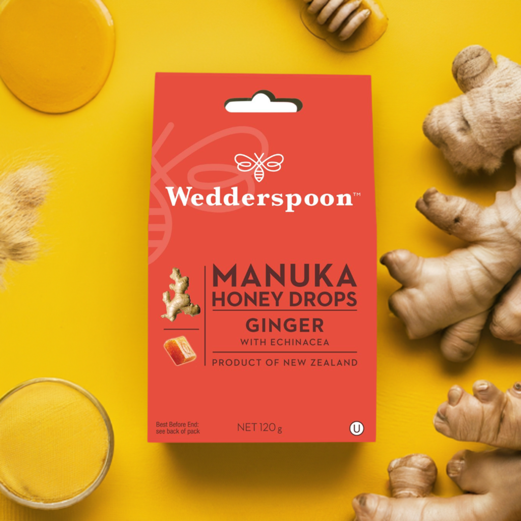 Wedderspoon throat lozenges red box on yellow background with fresh ginger roots and honey Manuka honey drops with ginger
