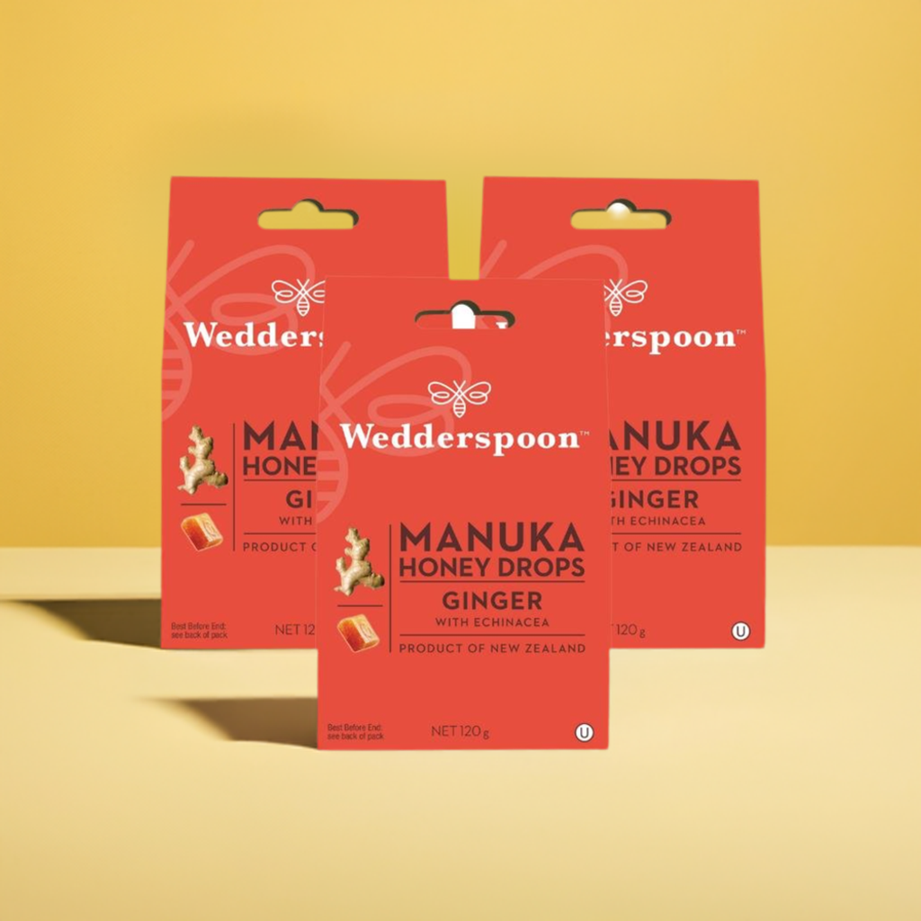 Wedderspoon Manuka honey drops with ginger throat lozenge boxes in red packaging on yellow background