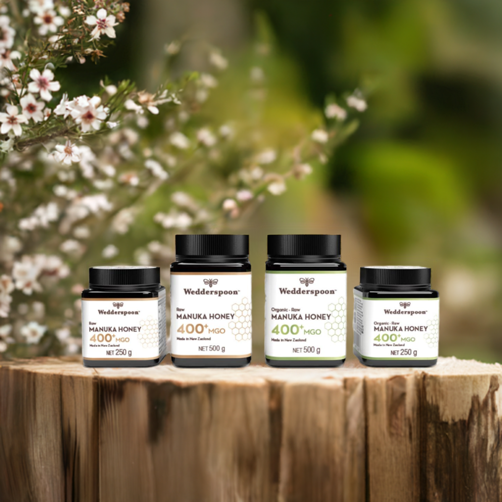 Wedderspoon jars of raw manuka honey 850 mgo displayed on wooden stump with manuka blooms