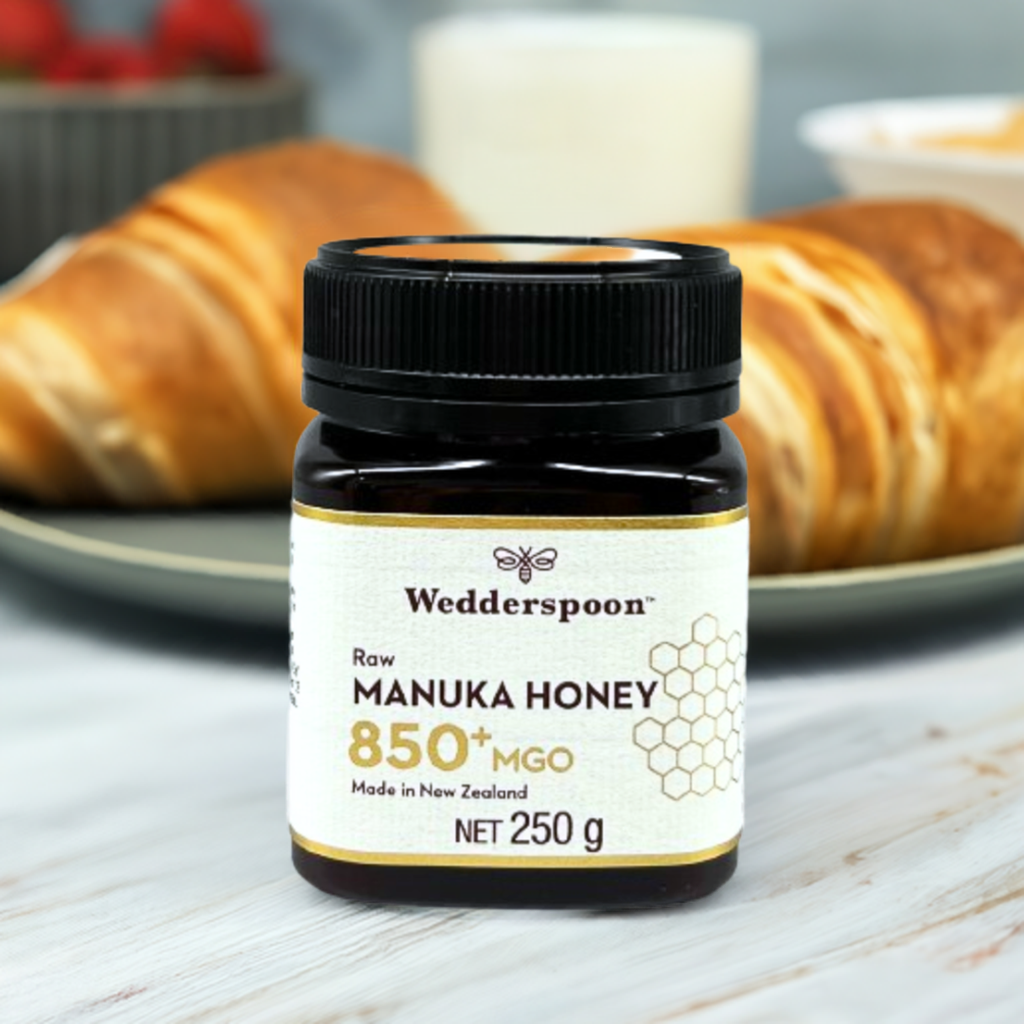 Wedderspoon jar of raw manuka honey 850 mgo on a breakfast table with croissants and a glass of milk