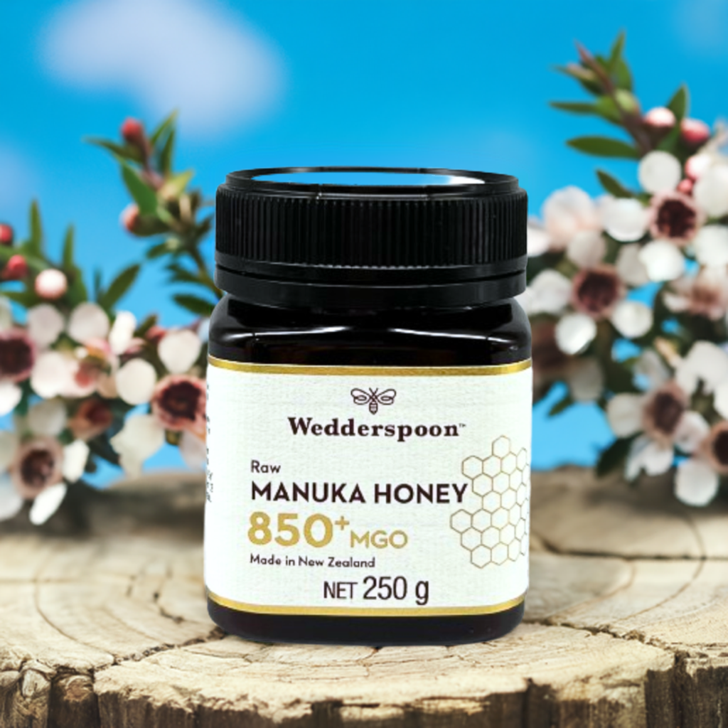 Wedderspoon jar of raw manuka honey 850 mgo on wooden stump with manuka flowers in background