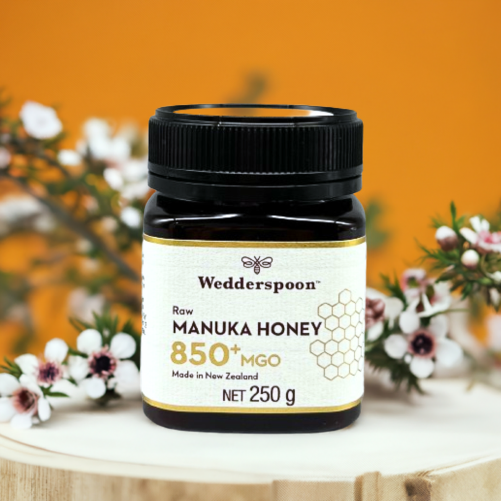 Wedderspoon jar of raw manuka honey 850 mgo 250 g on wooden stand with manuka flowers and orange background