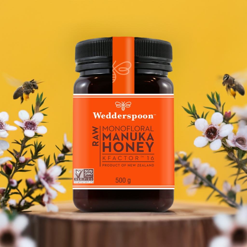 Wedderspoon raw Manuka honey KFactor 16 jar 500g with bees and flowers on wood surface