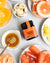 Wedderspoon raw Manuka honey KFactor 16+ jar on table with honey dipper and sliced citrus and bananas