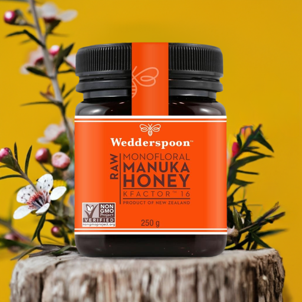 Wedderspoon raw Manuka honey KFactor 16+ 250 g jar with orange label on tree stump and manuka flowers