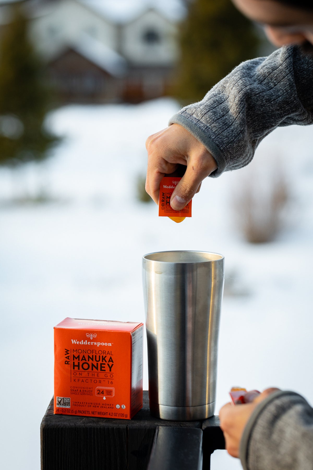 Wedderspoon raw Manuka honey travel sachets being poured into a stainless steel cup outdoors