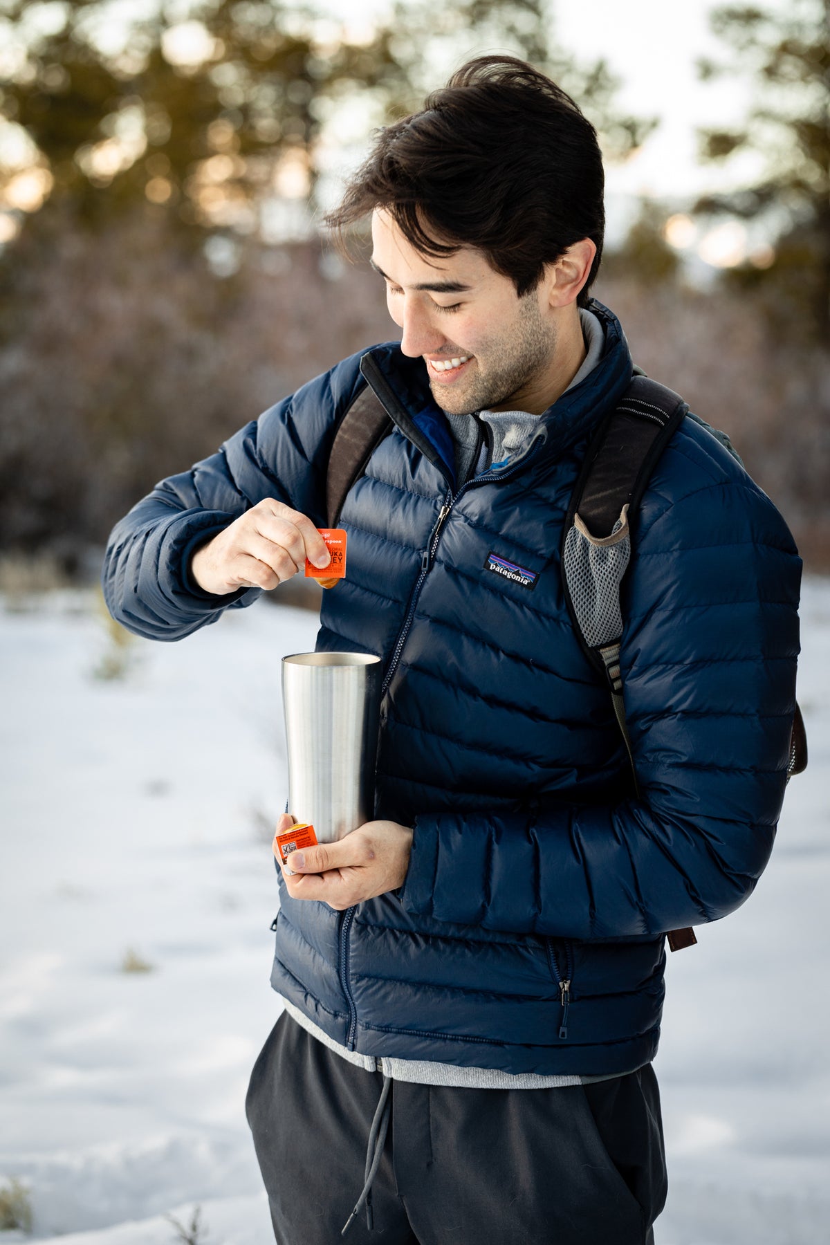 Man adding Wedderspoon raw Manuka honey travel sachets into a thermos outdoors in winter