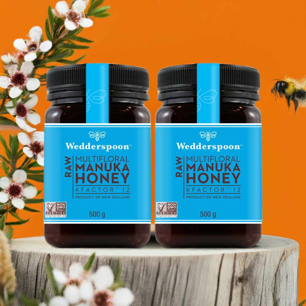 Two jars of Wedderspoon KFactor 12 honey Manuka honey on wooden surface with flowers and bee
