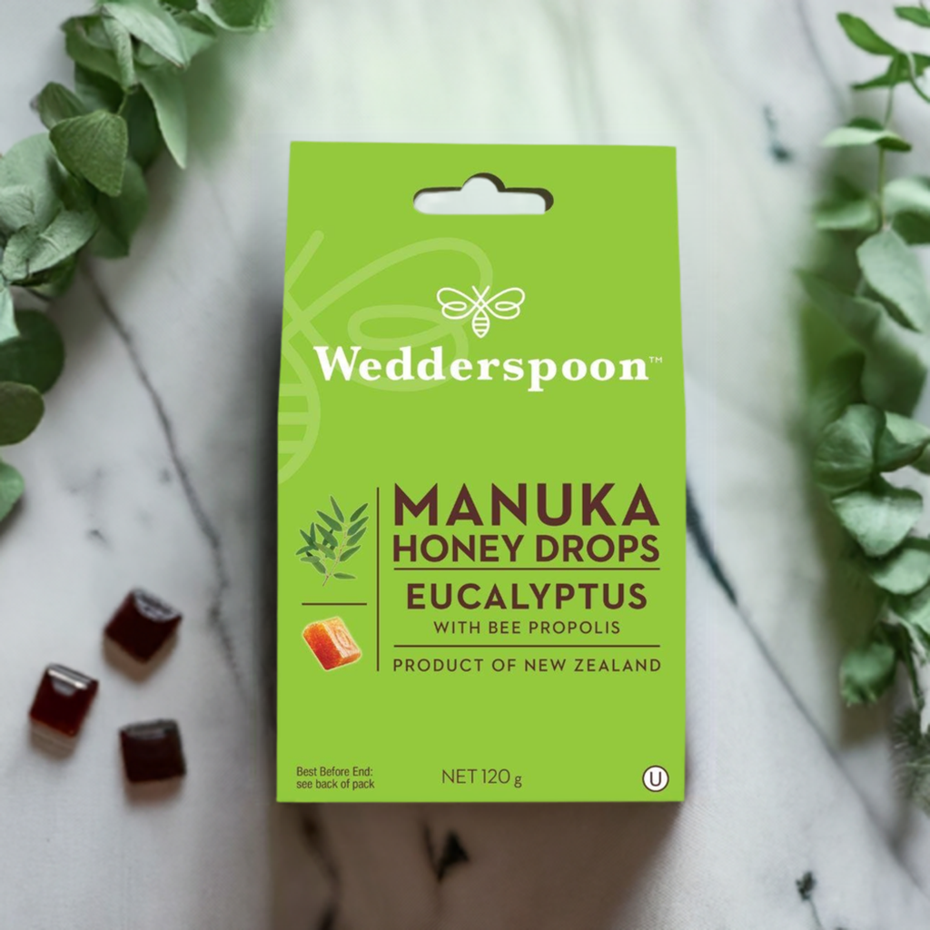 Wedderspoon Manuka honey drops eucalyptus throat lozenges in green box with eucalyptus sprigs and scattered lozenges